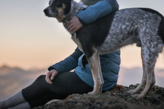 Women sitting and hugging a dog on top of a hill