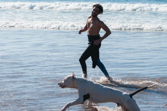 Man running with dog in ocean shore