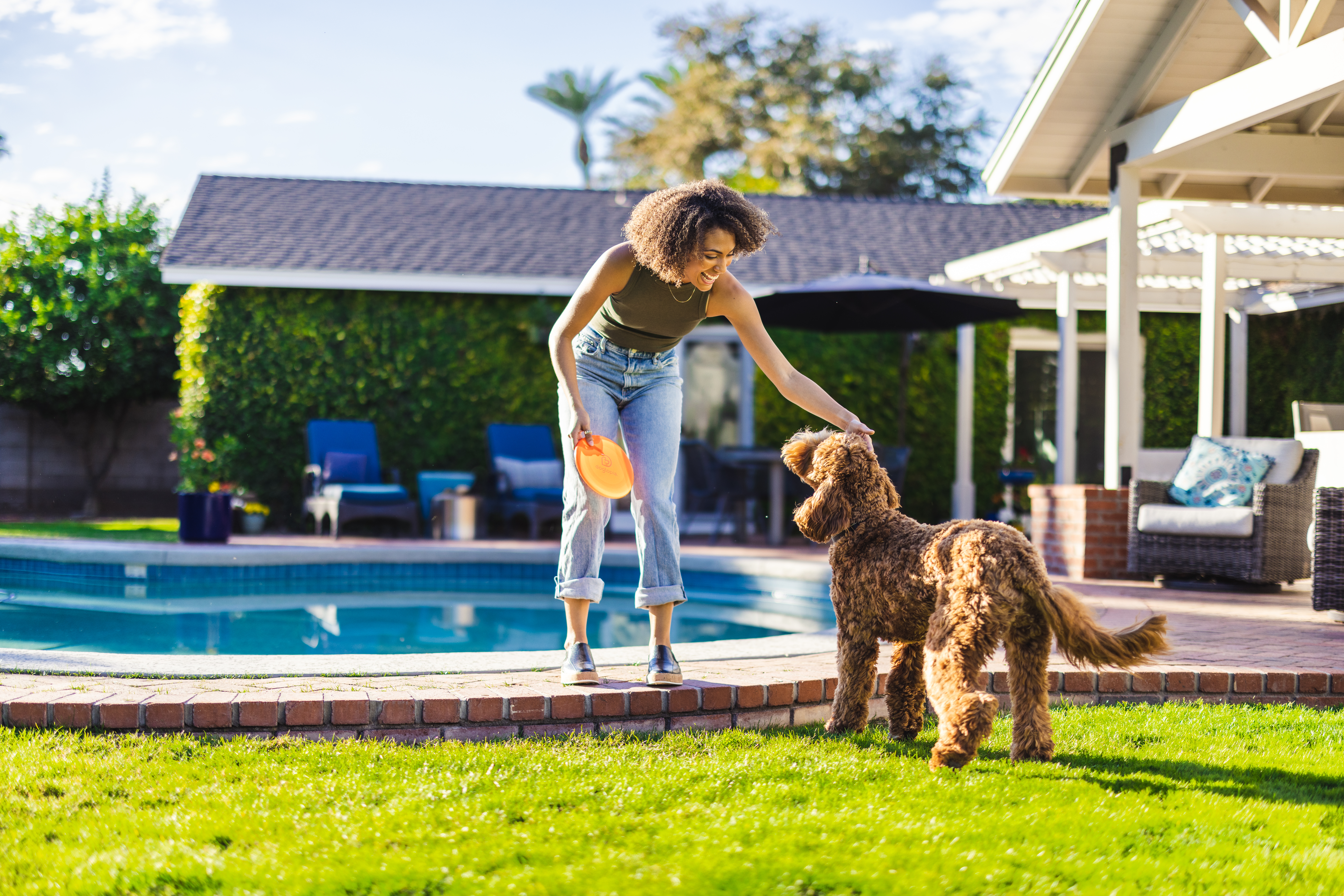 Woman petting dog holding an orange frisbee outside