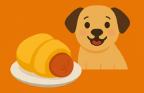 A playful cartoon-style illustration shows a smiling tan dog with floppy brown ears next to a white plate holding a 🐷🥐 Pigs in a Blanket snack. The snack features a reddish-brown sausage wrapped in golden crescent dough, with the end of the sausage exposed. Above the plate floats a pink pig face emoji with a round snout and small ears. The background is solid orange, creating a warm and cheerful vibe. No text is present in the image. Designed for visual accessibility and promotional use.