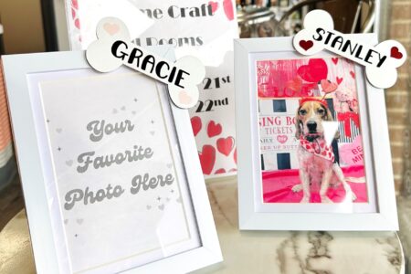 two white picture frames with white dog dones in the top corner that say Gracie and Stanley. Gracie's bone has two pink hearts and Stanley's bone has two red hearts on either side of their names. Stanley's frame is a picture of a beagle infront of a kissing booth and Gracie's says Your favorite photo here