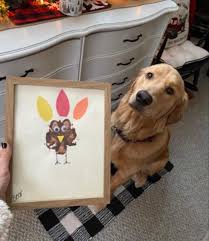 Dog is sitting in front of a person, looking at a paw painting made at daycare